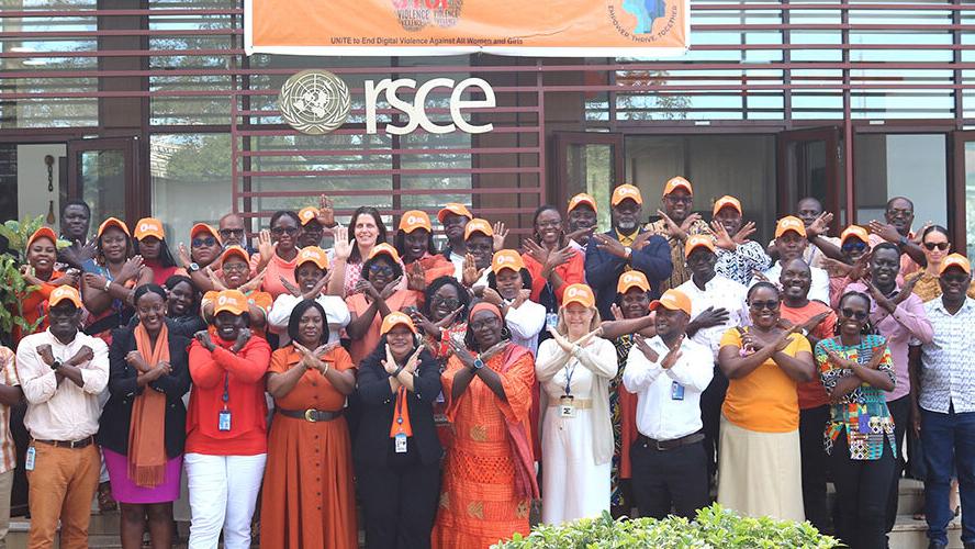 A group of people all wearing orange coloured clothing and hats all crossing their arms in the 'no' signal and smiling. 