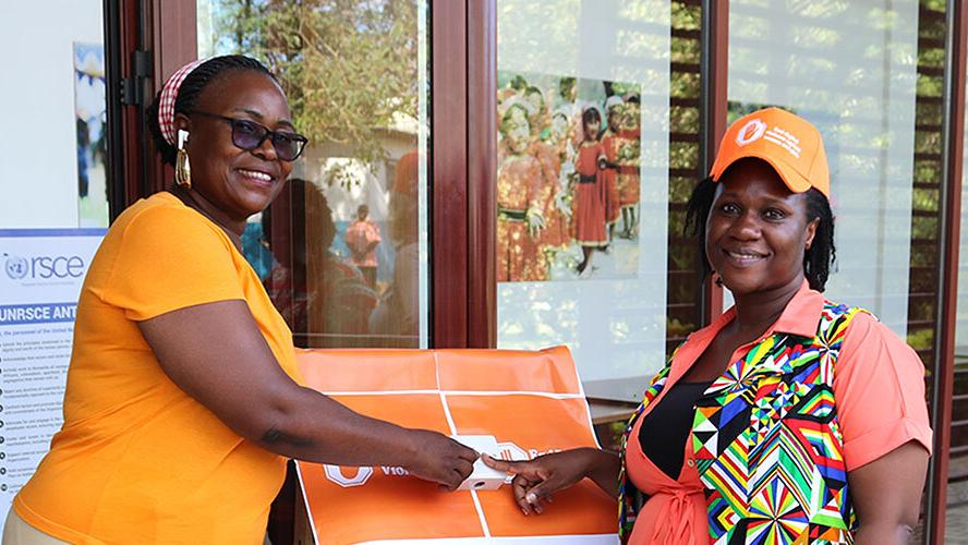 Two women both wearing orange coloured clothing and smiling each putting a finger on a button between them