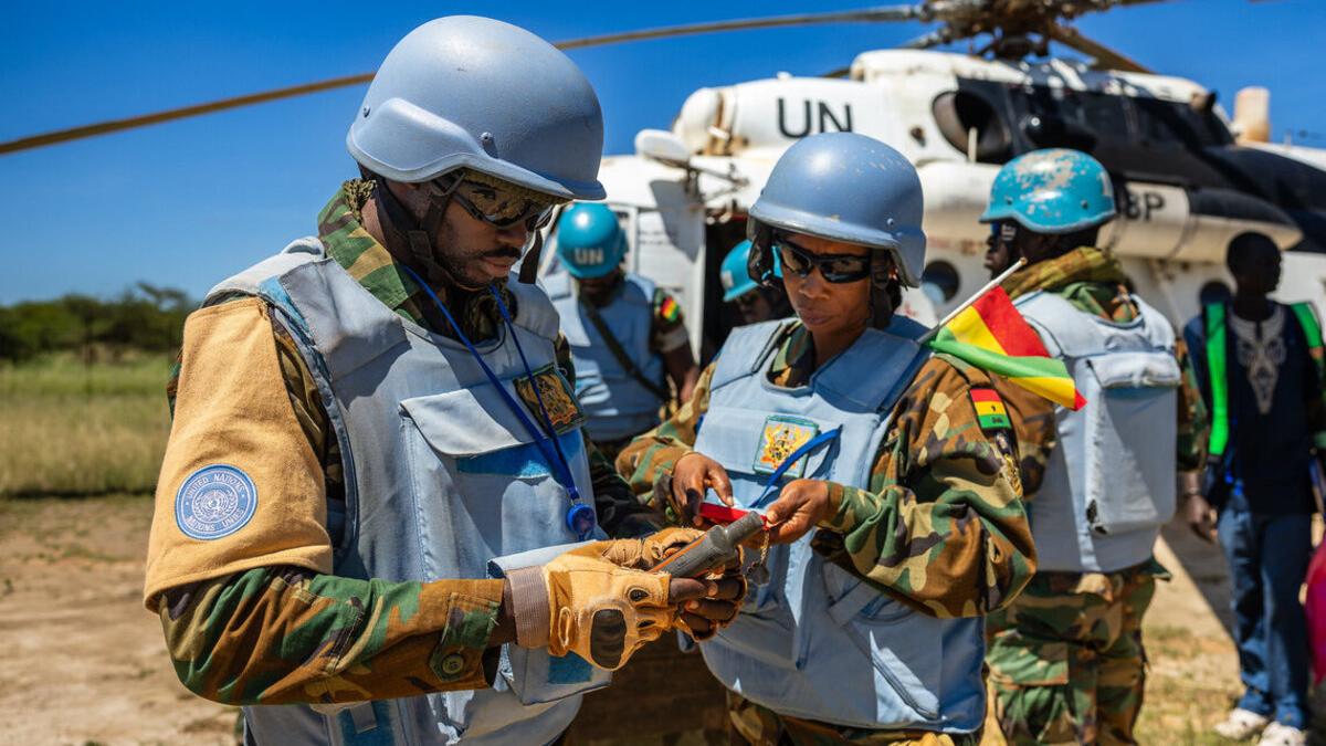 Two peacekeepers use technology devices in front of a UN helicopter.