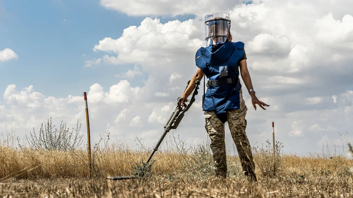 a female deminer is clearing the land with a detector