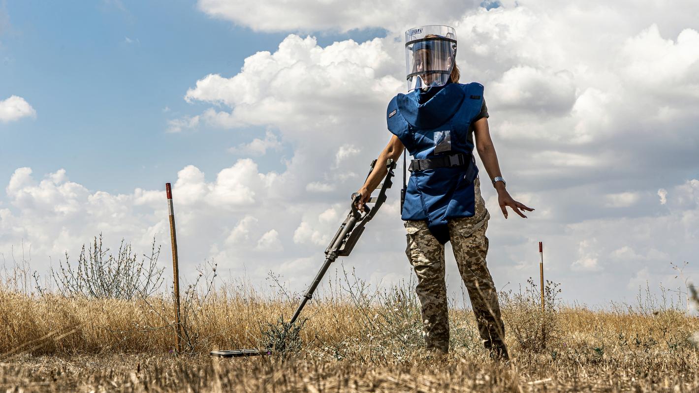 a female deminer is clearing the land with a detector