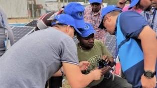 A group of people in blue baseball caps standing around working on an indeterminate piece of technology