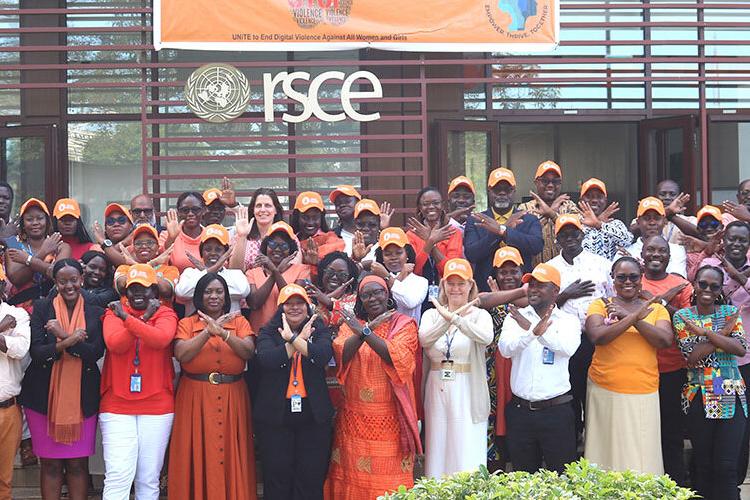 A group of people all wearing orange coloured clothing and hats all crossing their arms in the 'no' signal and smiling. 