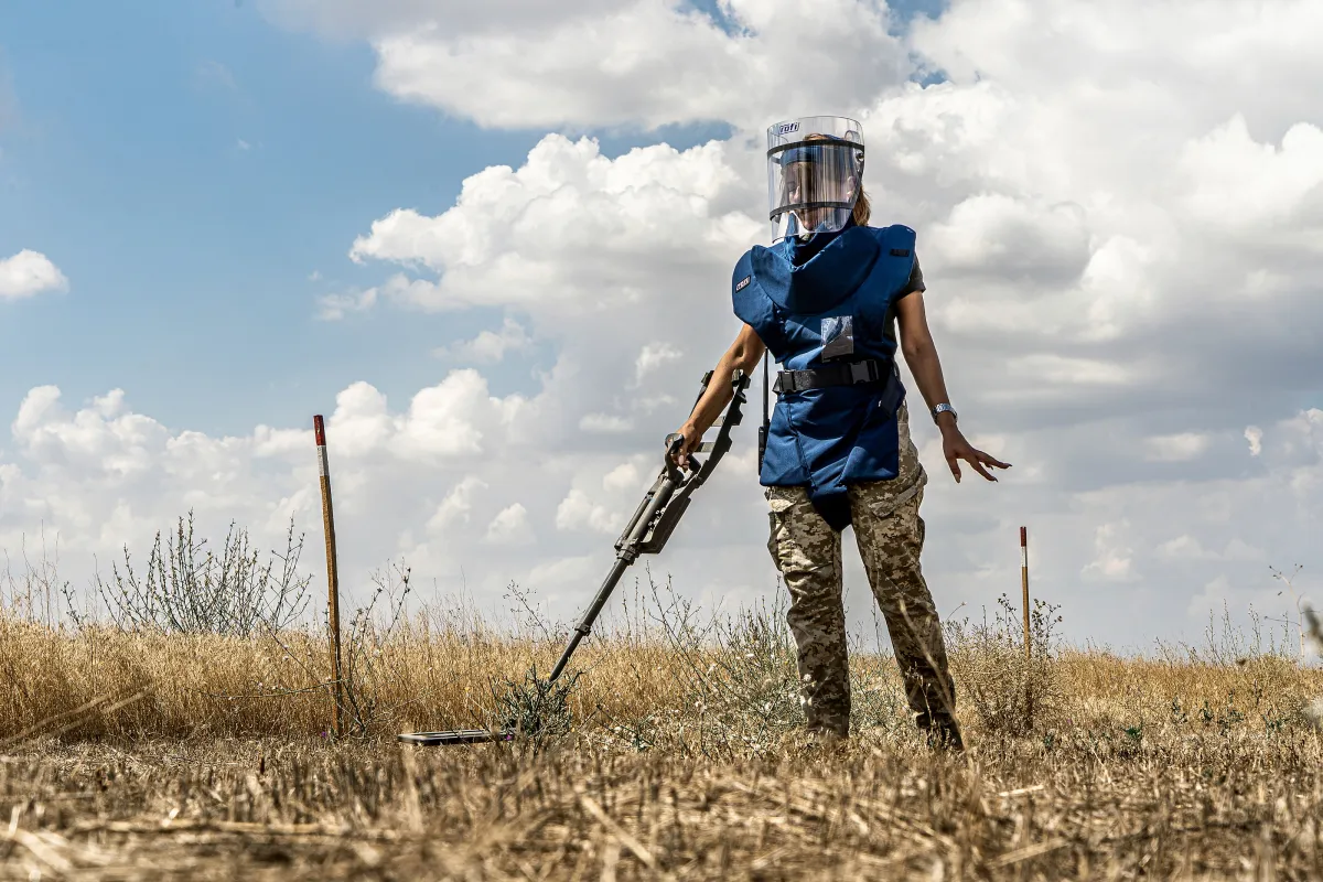 a female deminer is clearing the land with a detector