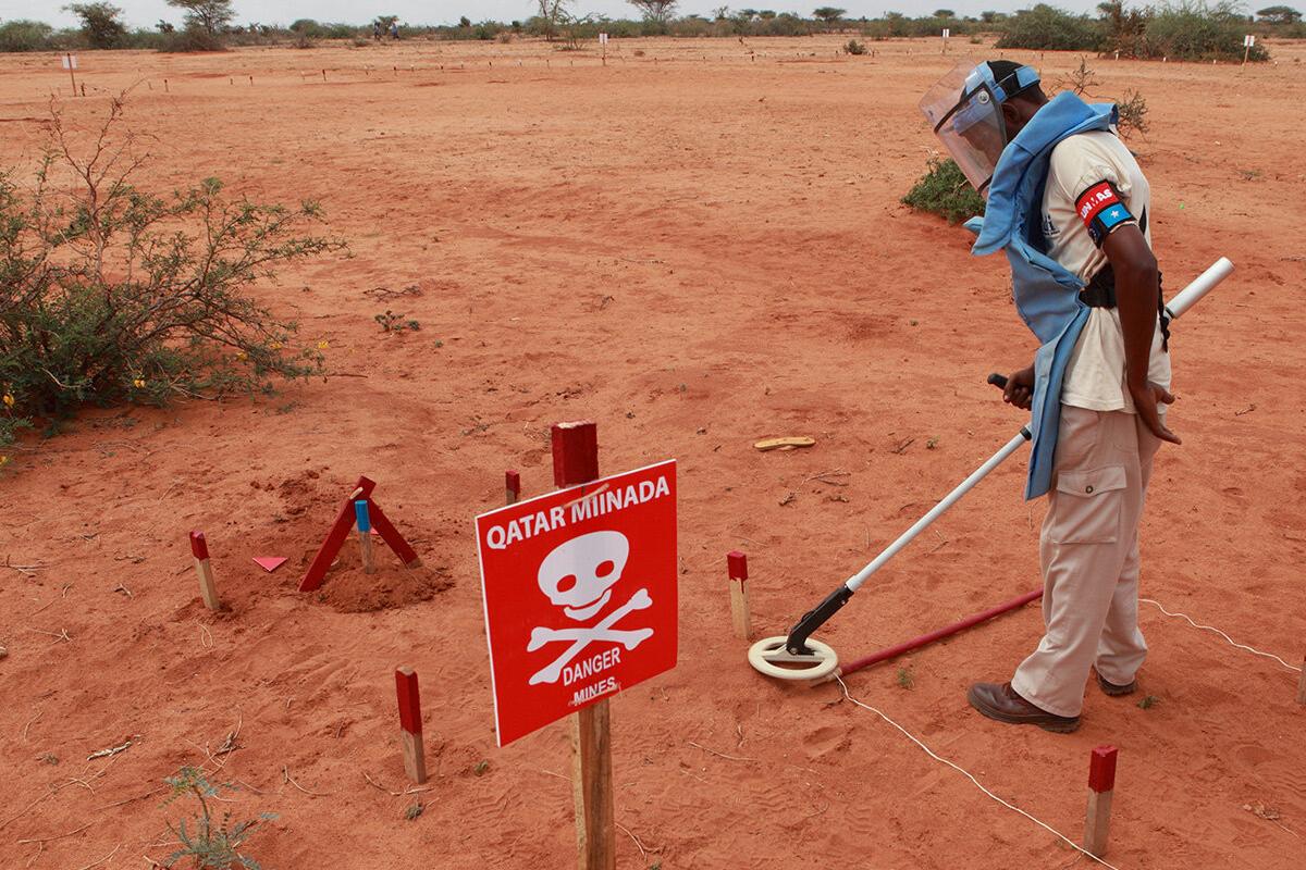 a deminer is deminig the field with a detector with a red sign beside.