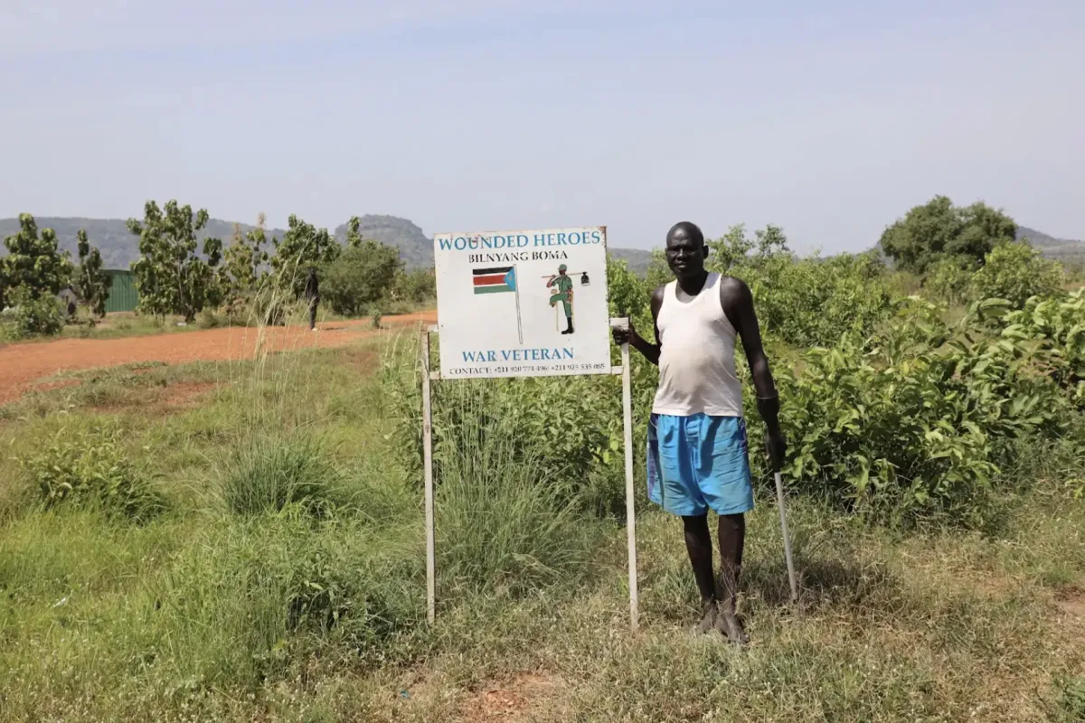 A member of the Wounded Heroes farming group stands beside the group’s sign in Bilinyang Payam, Central Equatoria State. The group consists of internally displaced, conflict-injured former soldiers who now farm on land cleared by UNMAS