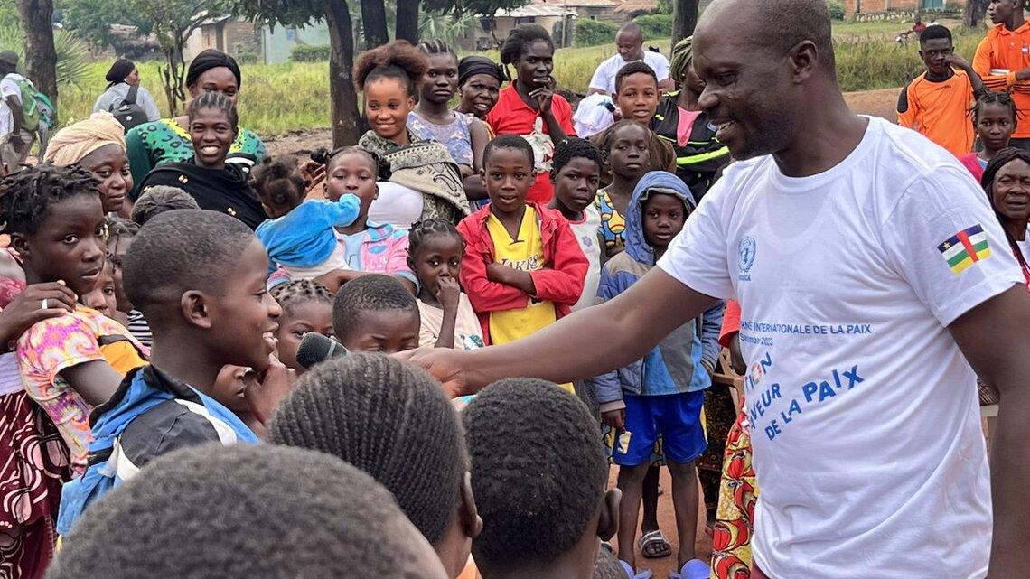 A peacekeeper in civilian clothes holds a microphone out to a young person in a crowd of young community members