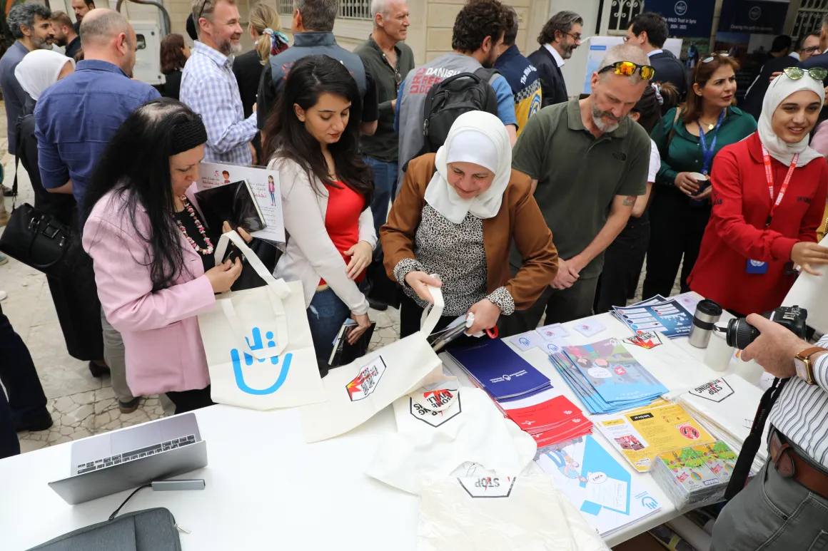 A group of people are standing in front of a booth, looking at the brochures on the table.