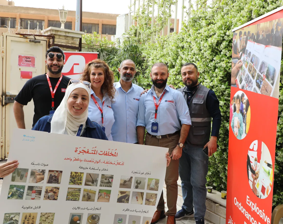 Six people are standing together beside a red banner