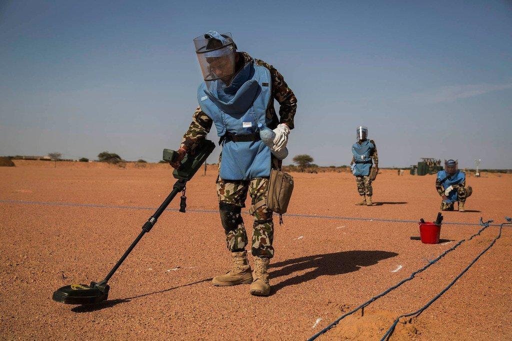 Three UN peacekeepers sweep for mines in a desert