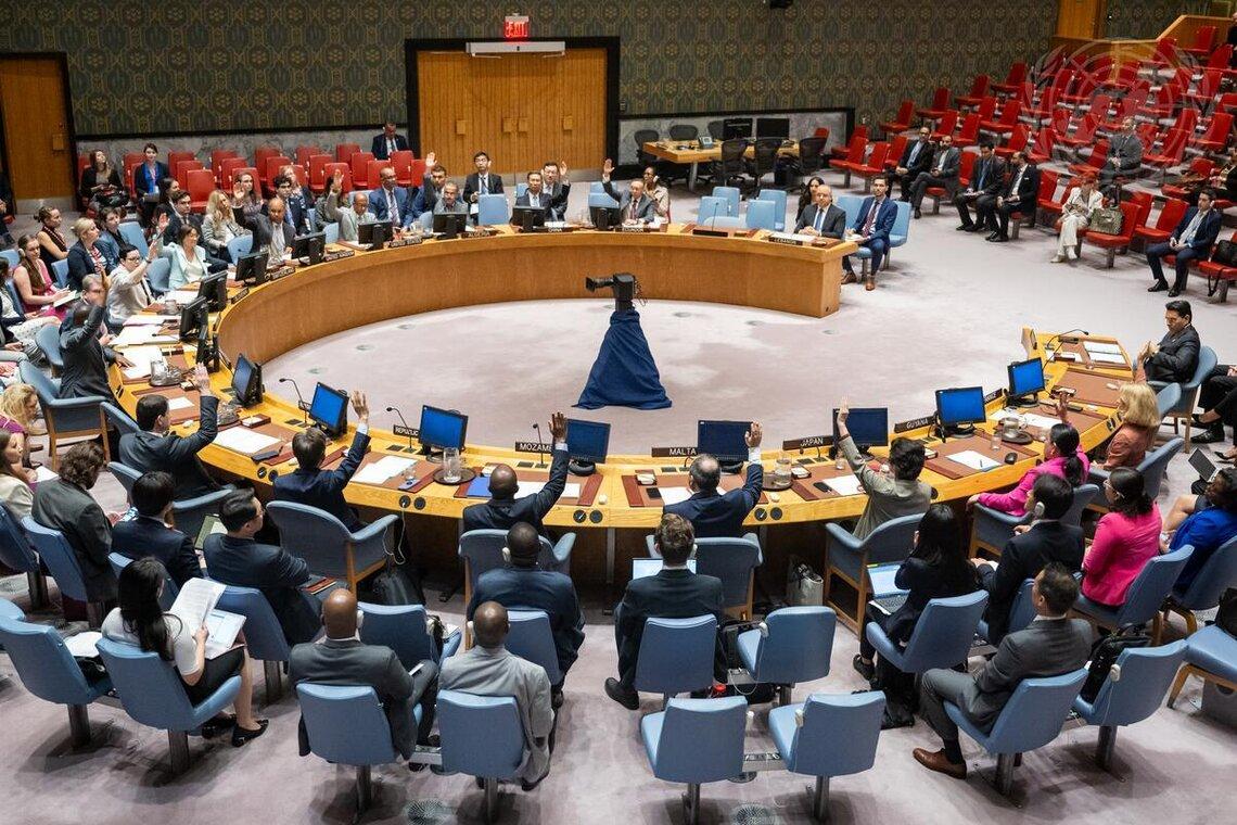 Des représentants des États Membres sont assis sur des chaises disposées en cercle dans une grande salle et lèvent la main.